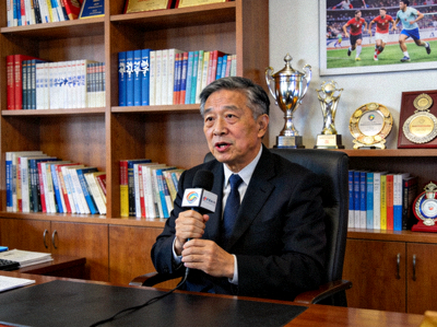 体育科学专家王教授 - 在办公室接受采访，背景是书架和体育奖项