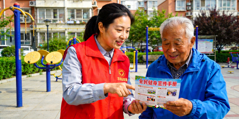 社区志愿者向居民发放全民健身宣传手册，讲解运动知识
