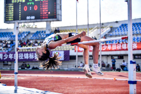 青少年田径锦标赛跳高赛场，一位女运动员采用背越式成功越过横杆的精彩空中姿态