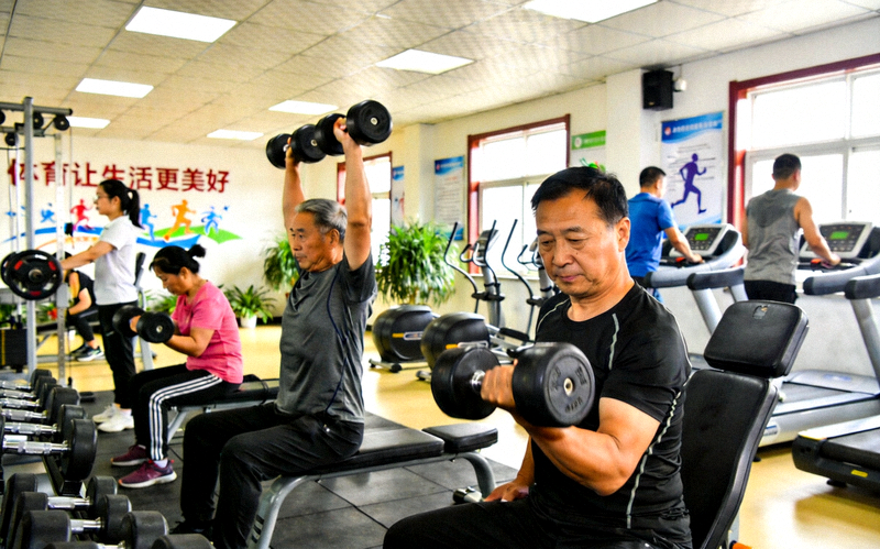 健身房内市民使用哑铃与器械进行力量训练，践行体育让生活更没好的场景