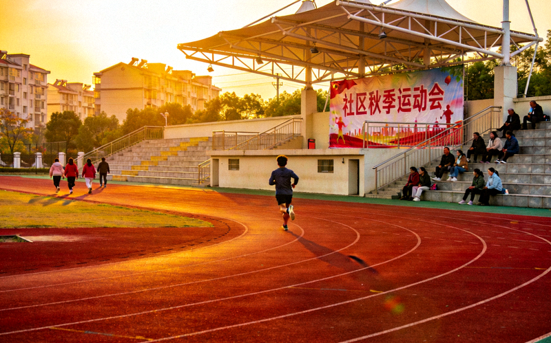 夕阳下的体育场跑道与看台，呈现社区体育赛事举办场地